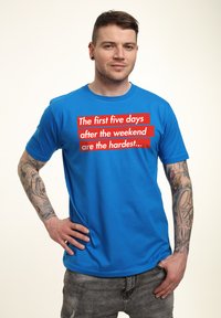 Camiseta de algodón azul con manga corta que presenta un texto rojo: "Los primeros cinco días después del fin de semana son los más difíciles..." en el frente.