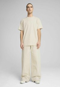 Beige oversized t-shirt med et lille grafik, parret med brede beige bukser. Blødt, åndbart stof med subtil tekstur. Hvide sneakers.