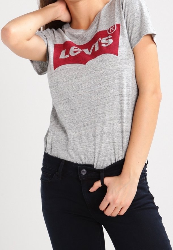 Femme portant un t-shirt gris Levi's et un jean noir, une main derrière la nuque et l'autre ajustant la taille du jean.