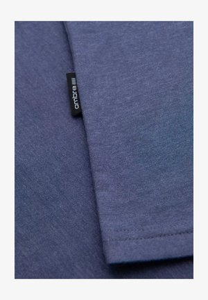 T-shirt in cotone blu scuro con texture liscia. Presenta un piccolo etichetta nera con il marchio "ombre" vicino alla cucitura.