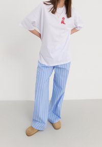T-shirt blanc oversize avec un motif de botte rouge, associé à un pantalon large à rayures bleu clair et à des chaussures beige sans lacets.