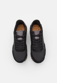 Chaussures de sport noires en tissu texturé et daim, avec une semelle intérieure en liège, des lacets ronds et une semelle extérieure en caoutchouc pour une bonne adhérence.