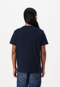 T-shirt en coton bleu marine avec un col rond classique, des manches courtes et une coupe décontractée, associé à un jean en denim effiloché.