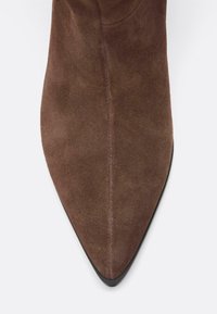 Bottine en daim marron avec bout pointu, texture lisse et semelle en caoutchouc noire. Présente un design sans coutures ni éléments métalliques visibles.