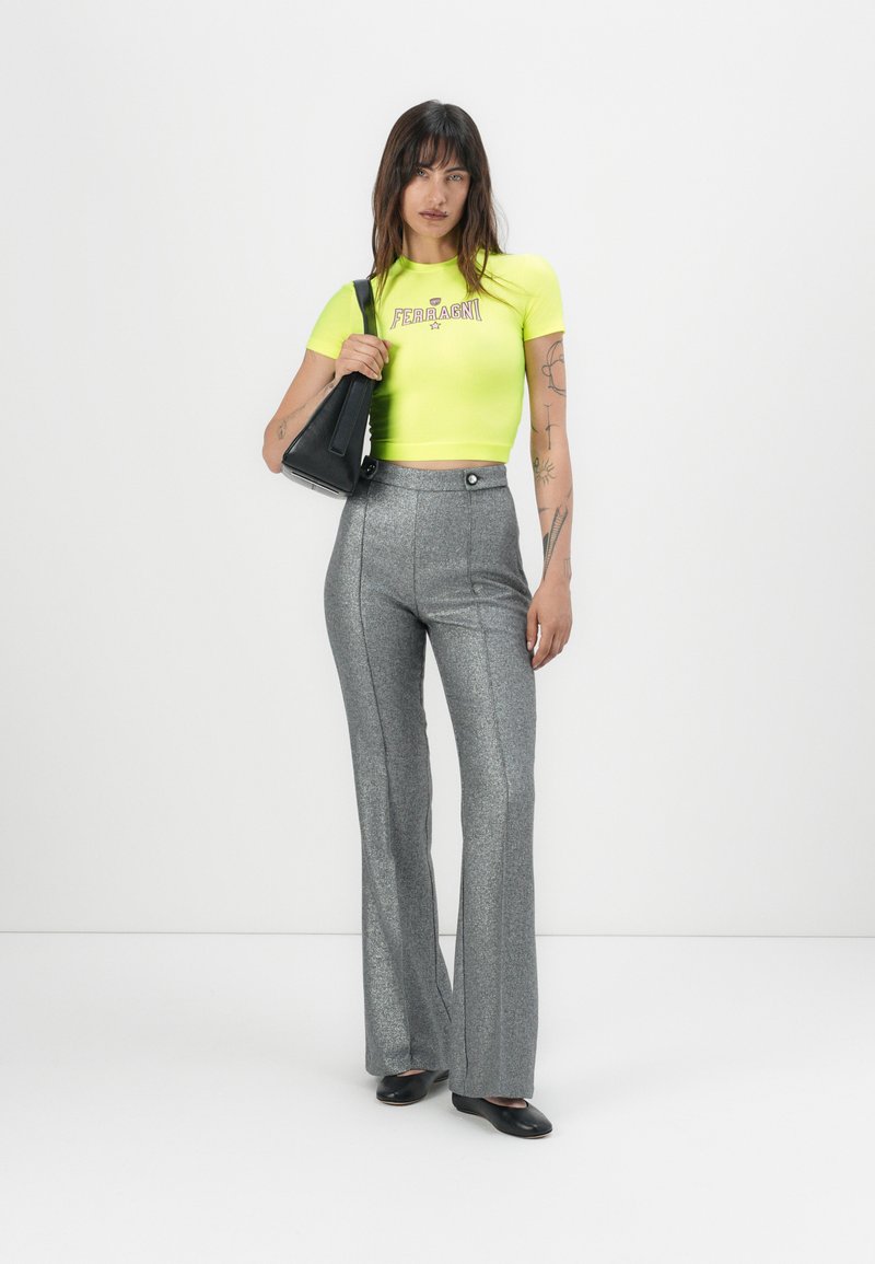 Camiseta corta de color amarillo neón con logo, combinada con pantalones acampanados de purpurina plateada y un bolso negro, con cintura alta y textura suave.