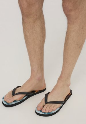 Infradito neri con cinturini texturizzati, caratterizzati da una soletta colorata e decorata e una suola nera spessa, indossati su piedi nudi.