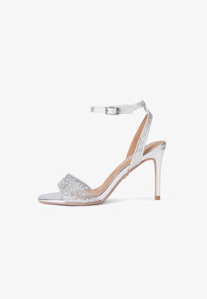 Zilveren sandalen met hoge hak, enkelbandje, open teen en strassversieringen op de bandjes en hak.