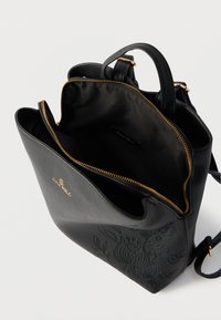 Μαύρο δερμάτινο σακίδιο με ανάγλυφο λουλουδένιο σχέδιο, χρυσό φερμουάρ μερικώς ανοιχτό που αποκαλύπτει το άδειο εσωτερικό και μικρή ετικέτα με την επωνυμία στο εσωτερικό.