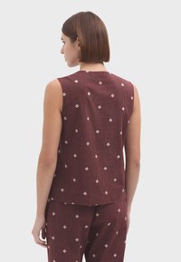 Haut sans manches bordeaux avec une texture côtelée et des motifs en damier crème. Coupe simple et droite avec un encolure arrondie à l'arrière.