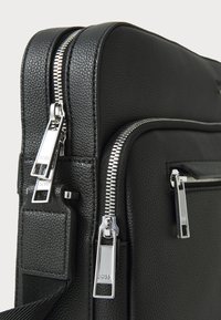 Borsa in pelle nera texturizzata con accessori in argento, dotata di due zip e attacco per tracolla. Forma compatta e rettangolare.