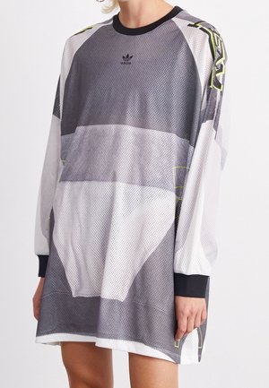 Persona con un vestido de malla Adidas de manga larga y talla grande, con patrones geométricos en negro, blanco y gris y detalles en amarillo neón.