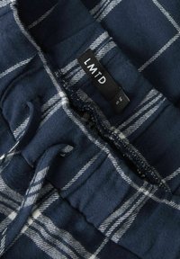 Pantalons de pyjama en flanelle bleu marine avec un motif à carreaux blancs, dotés d'une taille élastique et d'un cordon de serrage pour un ajustement réglable. Étiquette portant la mention "LMTD."