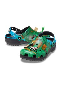 Groene plastic klompen met een structuur oppervlak, voorzien van een kleurrijk patroon, zwarte zool en decoratieve accenten in verschillende kleuren en vormen.