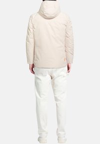 Lichtbeige gewatteerd jack met capuchon, gemaakt van glad materiaal. Voorzien van een strak ontwerp en een subtiele oranje accent bij de zoom. Gecombineerd met witte broek.