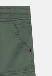 Zelené bavlněné kalhoty s texturovaným pasem, šikmými kapsami a kovovým zapínáním. Hladká tkanina s viditelnými švy.