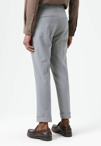 Pantalon gris clair à coupe ajustée, ourlets retroussés, deux poches arrière, associé à des mocassins marron et une chemise beige.