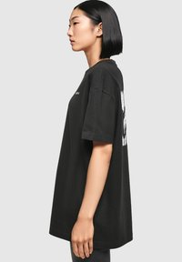 Sort bomulds T-shirt med løs pasform, korte ærmer og hvid grafisk tekst på ryggen, vist fra siden.
