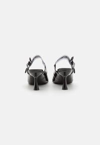 Scarpe con tacco in pelle verniciata nera con design slingback, caratterizzate da una cinghia bianca a contrasto con dettagli del logo e un sottile tacco a stiletto.