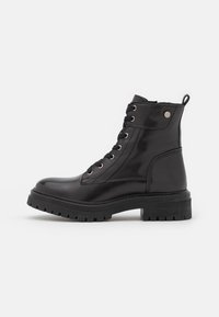 Botas de tobillo negras con cordones, hechas de cuero pulido, que cuentan con ojales metálicos, una suela de goma texturizada y una asa en la parte posterior.