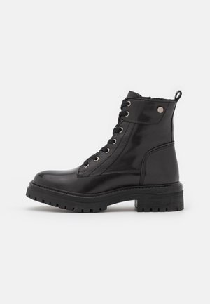 Black lace-up ankle boots made of polished leather, featuring metallic eyelets, a textured rubber sole, and a pull tab at the back.