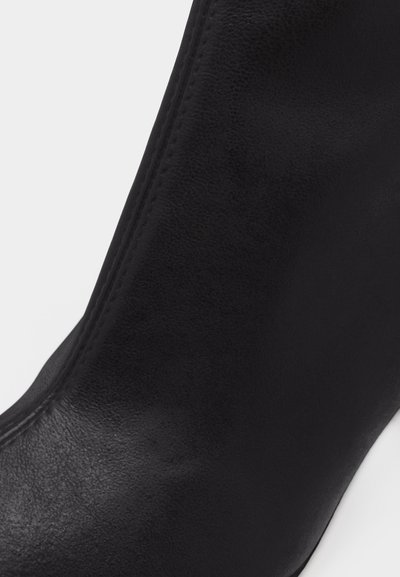 Κοντινή λήψη μαύρης δερμάτινης μπότας με ομαλή υφή και λεπτομερή ραφή κατά μήκος της πλαϊνής ραφής.