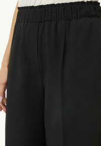 Black, wide-leg trousers with a smooth texture, elastic waistband, and side pockets, featuring a tailored fit and clean lines.