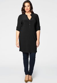 Sorte tunika med lange ærmer, knaplukning og opsmøgede manchetter, parret med mørke skinny jeans og metalliske spidse flade sko.
