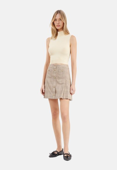 Top senza maniche color crema abbinato a una gonna a quadri beige con bottoni frontali. La gonna ha un orlo svasato e una leggera texture. Le scarpe basse nere completano il look.