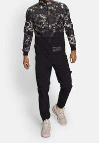 Giacca zip tie-dye in bianco e nero con parte inferiore nera, abbinata a pantaloni jogger neri. Presenta tasche cargo e sneakers leggere.