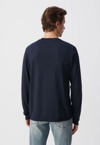 Marineblaues Langarm-T-Shirt aus weicher Baumwolle, mit Rundhalsausschnitt und lockerer Passform, getragen über hellblauen Jeans.