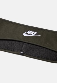 Olive žalia Nike galvos juosta su balta logo, pagaminta iš minkštos medžiagos; turi pūkinę vidinę dalį šilumai ir komfortui.