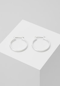 Silver hoop earrings with a smooth, circular design and a thin profile. The closure is a simple hook style. Set against a light background.