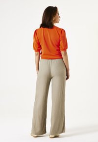 Rode top met korte mouwen en puffed sleeves; lichtgewicht beige wijdlopende broek van een vloeiende stof. Model wordt van achteren getoond.