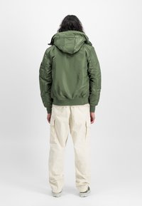 Olive green padded jacket with a hood, ribbed cuffs, and hem. Paired with cream cargo pants featuring side pockets and loose fit.