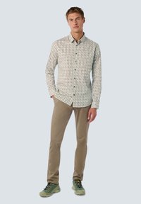 Heren overhemd met knopen in een lichte crèmekleur, voorzien van een veelkleurig geometrisch patroon. Gecombineerd met beige broeken en groene schoenen.