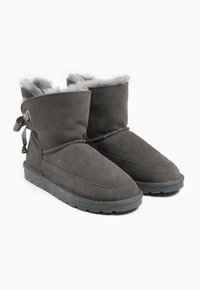 Botines de ante gris con un suave forro de piel, que cuentan con un lazo decorativo y una suela de goma resistente. Textura suave y diseño de punta redonda.