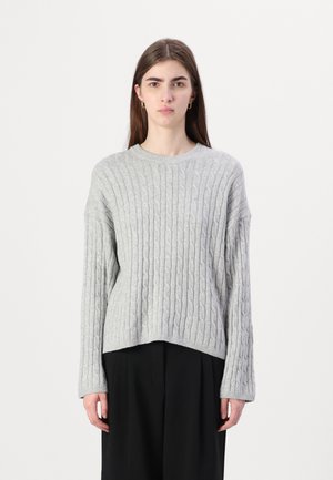 Pull en tricot gris avec des manches longues, un col rond et un ourlet légèrement court. La texture est douce et côtelée, ajoutant de la dimension.
