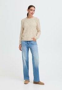 Beige strikket genser med teksturert mønster, kombinert med lyseblå rette jeans og beige slip-on sko. Enkel design.