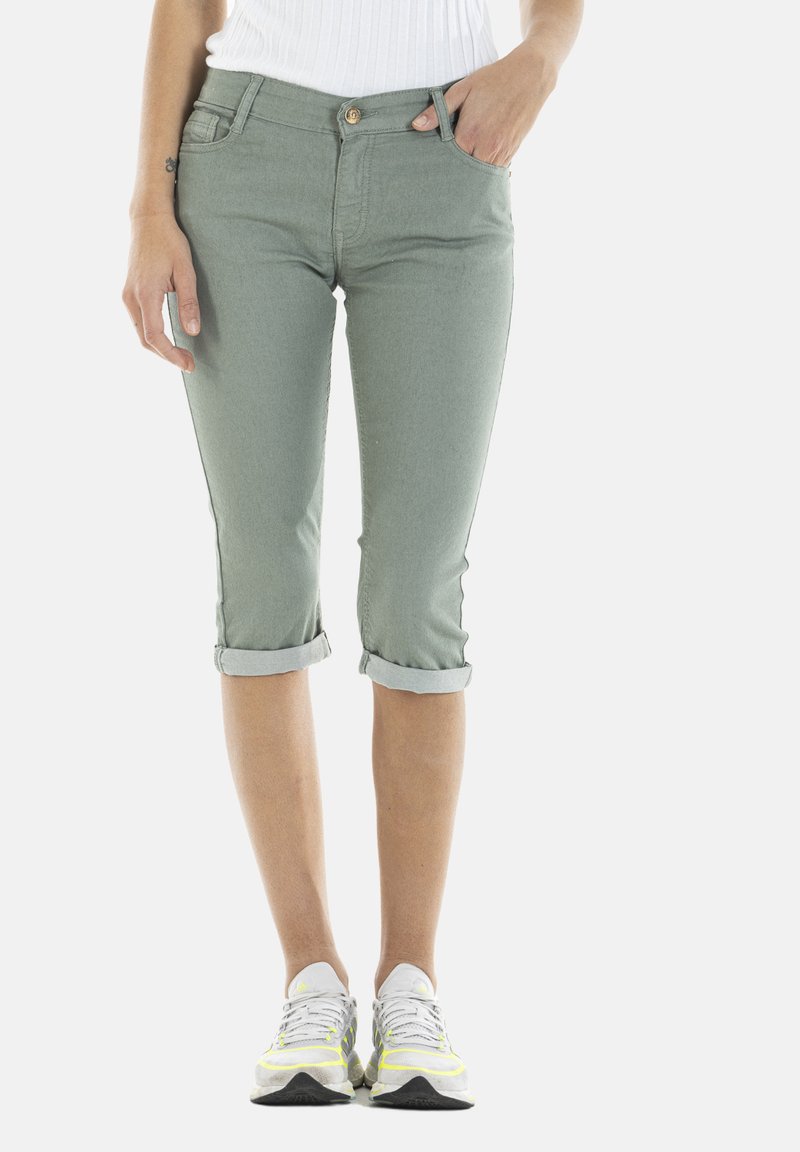 Pantalons capri vert clair en denim, avec des revers retroussés, une poche avant et une fermeture à bouton doré. Associés à des baskets blanches et grises.