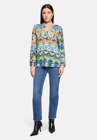 Kolorowa, wzorzysta bluzka z dekoltem w serek i długimi rękawami, w zestawieniu z niebieskimi jeansami o prostych nogawkach oraz czarnymi szpilkami z zaostrzonym noskiem.