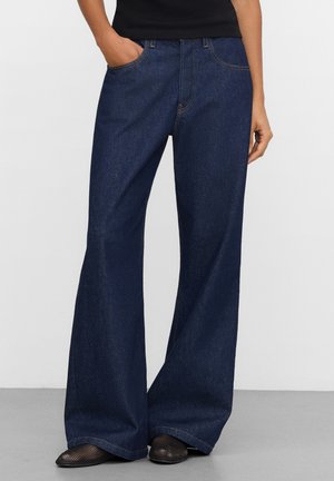 Granatowe dżinsy o szerokich nogawkach wykonane z denimu, z wysokim stanem, przednimi kieszeniami oraz widocznym przeszyciem dla dodatkowego efektu.