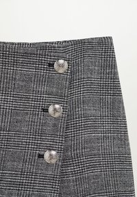 Jupe à carreaux en tissu noir et gris, ornée de trois boutons métalliques, présentant une surface texturée avec une coupe structurée.