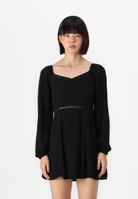 Melna kleita ar garām puffed piedurknēm, kvadrātveida izgriezumu un mežģīņu apdari. Plūstoša auduma A-silhouette ar viļņotām apakšmalām.