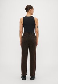 Svart ermeløs topp kombinert med høyt liv, mørkebrune denim-bukser med rett ben og buede baklommer.