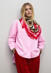 Camisa rosa de manga larga con pu�ños de estampado de leopardo, combinada con una bufanda de múltiples patrones que presenta acentos en rojo, beige y negro. Pantalones rojos.