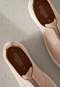 Vaaleanpunaiset mokka slip-on kengät, joissa on valkoinen pohja, pyöreä kärki ja minimaalinen ommel. Sisäpuolella on ruskea nahkavuori ja brändäys.