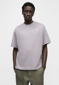 Ανοιχτό μοβ κοντομάνικη μπλούζα με στρογγυλή λαιμόκοψη και μικρό λευκό λογότυπο στο αριστερό στήθος, κατασκευασμένη από ομαλή, απαλό ύφασμα.