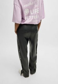 Zwarte faux leren broeken met drukknoopsluitingen aan de zijkanten, met een gladde textuur en elastische tailleband, gecombineerd met een lichtpaars t-shirt.