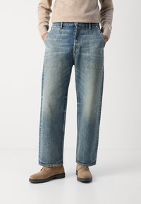 Lyseblå denim vide bukser med to frontlommer, falmet tekstur og rå kant, kombinert med brune semskede ankelsko.