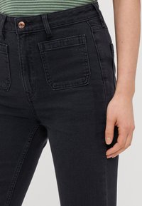Pantalones vaqueros negros de tiro alto con una textura suave, que cuentan con dos bolsillos traseros y un botón de cobre en la parte frontal.